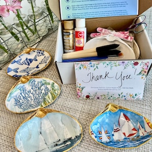 May include: A craft kit for decoupaging shells, featuring various seashell-shaped dishes with nautical and marine-themed designs. The kit includes Mod Podge, paint, brushes, and instructions. The shells have gold trim and are decorated with sailboats and fish.