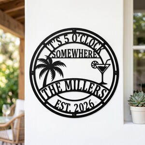 Könnte beinhalten: Ein rundes Wand-Schild aus schwarzem Metall mit dem Text IT'S 5 O'CLOCK SOMEWHERE, THE MILLERS und EST. 2026. Das Design zeigt die Silhouette einer Palme und eines Cocktailglases mit Strohhalm, eingefasst in einen kreisförmigen Rahmen.