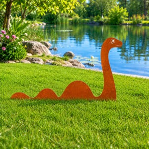 May include: A flat, rust-colored metal garden sculpture shaped like a long-necked sea creature. The silhouette features a tall, curved neck with a simple eye detail and three rounded humps along the body, designed to be placed in grass.