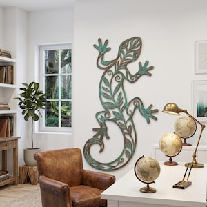 Puede incluir: Una gran pieza de arte mural de metal con forma de lagarto, con un acabado desgastado en color turquesa y marrón. El lagarto presenta un diseño en forma de hoja. La imagen también muestra un sillón de cuero, globos terráqueos y una lámpara de escritorio.