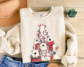 May include: A sand-colored sweatshirt featuring a graphic of six polar bears decorated with Christmas lights and festive accessories. The bears are arranged in a pyramid shape, creating a holiday theme.