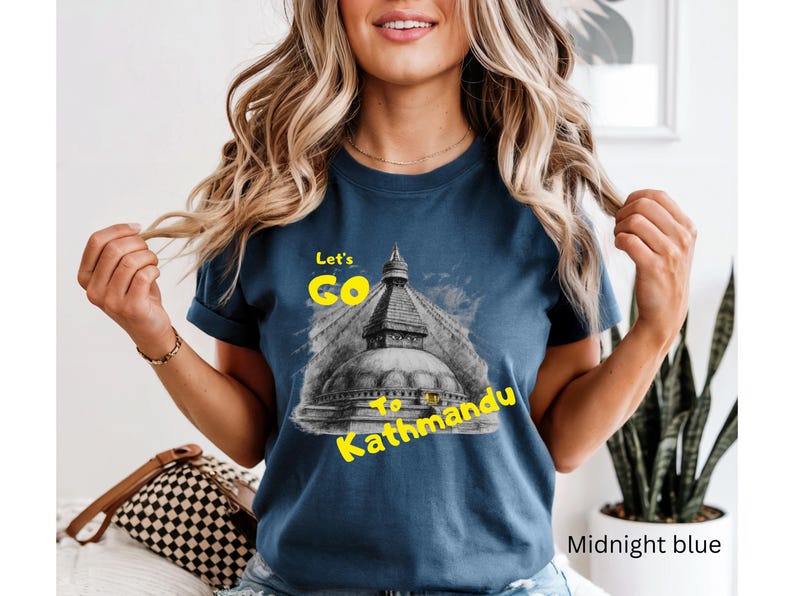 May include: Midnight blue t-shirt with a graphic of a Nepalese stupa and the text "Let's Go to Kathmandu" in yellow. The shirt is a crew neck and has short sleeves.
