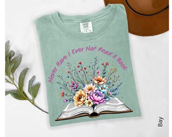 May include: A sage green t-shirt with the text "Never Have I Ever Not Read A Book" in a circular design. The shirt features an open book with a colorful floral arrangement of orange, pink, and blue flowers.