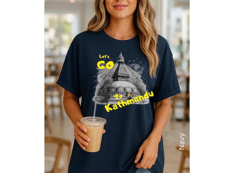 May include: Navy blue t-shirt with a graphic of a temple and the text "Let's Go to Kathmandu" in yellow. The image is of a woman holding a beverage.