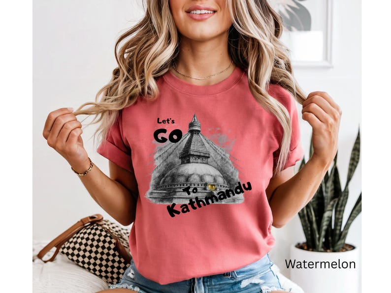 May include: A watermelon-colored t-shirt with the text "Let's Go To Kathmandu" in black. The graphic features a grayscale image of a temple. The shirt is a short-sleeved crew neck.