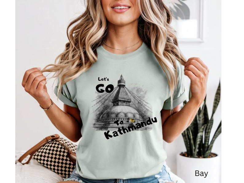May include: A light green t-shirt with the text "Let's Go To Kathmandu" and a black and white illustration of a temple. The shirt is a short-sleeved crew neck.