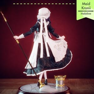 Pu&ograve; includere: Statuetta di una cameriera, con un vestito bianco e nero, grembiule e cuffia, che tiene una lancia. Un piccolo secchio dorato &egrave; sulla base. Il testo "Maid Kronii Hololive" &egrave; su un'etichetta verde.
