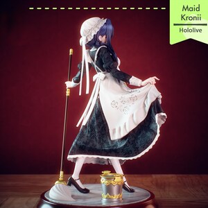 Pu&ograve; includere: Statuetta di una cameriera in abito bianco e nero, con una scopa. La statuetta ha i capelli blu e indossa un grembiule e un cappello bianchi. Sono visibili anche un secchio e la scritta "Maid Kronii Hololive".