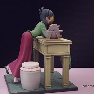 May include: A figurine of a woman in a green top and red skirt, leaning over a table with a grinding wheel. A white jar with a lid and a green base are in the foreground. The text "Maomao" is visible.