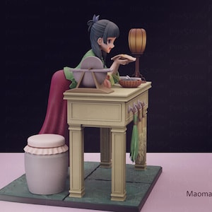 May include: A detailed figurine of a woman in traditional attire, leaning over a table with a lamp and basket. The figure is set on a green base, with a white stool nearby. The scene is rendered in soft, muted colors.