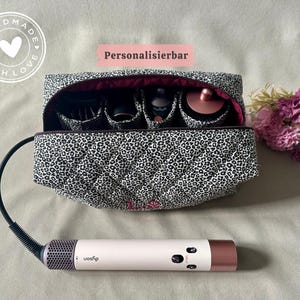 Può includere: Una borsa trapuntata con stampa leopardata e interno scuro contenente quattro accessori cilindrici per lo styling dei capelli. Uno strumento per lo styling dei capelli rosa chiaro e oro rosa metallizzato con cavo nero è posizionato davanti alla borsa.