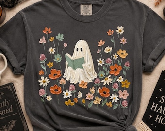 Könnte beinhalten: Ein anthrazitfarbenes Kurzarm-T-Shirt mit einer zentralen Grafik eines weißen Geistes, der ein grünes Buch liest, umgeben von einer bunten Anordnung gemalter Blumen in Orange, Gelb, Rosa und Weiß, inklusive eines Comfort Colors Etiketts.