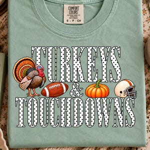 May include: A sage green t-shirt featuring the text "TURKEYS & TOUCHDOWNS" in a white font with black polka dots. The graphic includes a turkey, a brown football, an orange pumpkin, and a white football helmet with an orange stripe.
