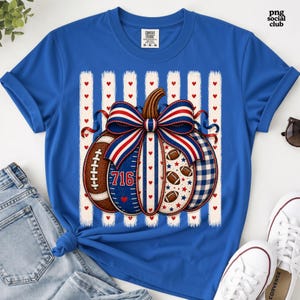 May include: A royal blue t-shirt featuring a central graphic of a pumpkin decorated with red, white, and blue patterns, footballs, and the number 716. The pumpkin is topped with a large striped bow and set against a background of vertical white stripes.