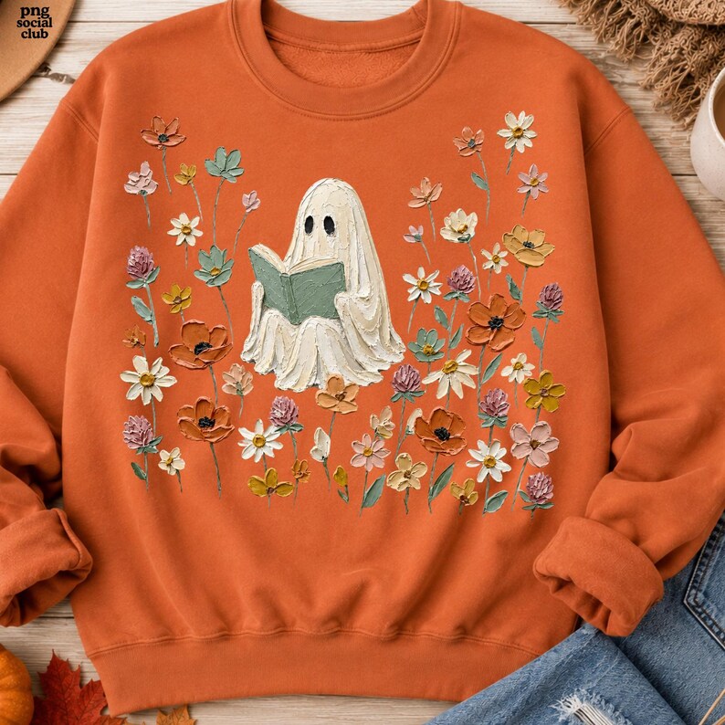 May include: An orange crewneck sweatshirt featuring a central graphic of a white ghost reading a green book, surrounded by a field of colorful wildflowers in shades of pink, yellow, orange, and teal, with the text png social club in the corner.