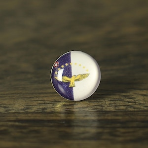 Peut inclure: Un bouton rond en verre avec un motif divisé en blanc et bleu foncé. Le côté bleu foncé comporte de petites étoiles jaunes, et le côté blanc présente un emblème d'aigle jaune. Le bouton est posé sur une surface à grain de bois foncé.