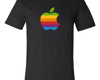May include: A black short-sleeve t-shirt featuring a centered graphic of an apple silhouette filled with horizontal stripes in green, yellow, orange, red, purple, and blue colors, with a small green leaf at the top of the apple shape.