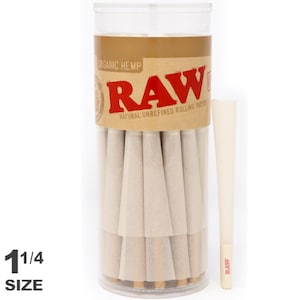 May include: A clear plastic tube containing pre-rolled, natural unrefined rolling papers. The tube has a brown label with the word "RAW" in red and the text "ORGANIC HEMP" and "NATURAL UNREFINED ROLLING PAPERS". A single pre-rolled paper stands beside the tube. The text "1 1/4 SIZE" is at the bottom.