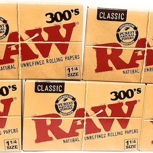 May include: Several boxes of RAW Classic natural unrefined rolling papers are stacked. Each box is tan with red text that reads "RAW" and "300's". The boxes are tied together with twine and feature the text "1 1/4 size".