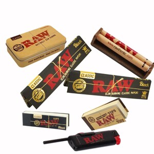May include: An assortment of RAW brand smoking accessories, including rolling papers, tips, a rolling machine, a lighter, and a metal tin. The packaging features the RAW logo in red on a black or tan background. The products are designed for rolling your own cigarettes.