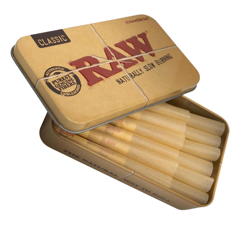 May include: A tan metal tin with the word "RAW" in red lettering and the text "NATURALLY SLOW BURNING". The tin is open, revealing several pre-rolled cones. The tin also has the text "CLASSIC" and "AUTHENTIC PUREST GENUINE FIBERS UNBLEACHED".