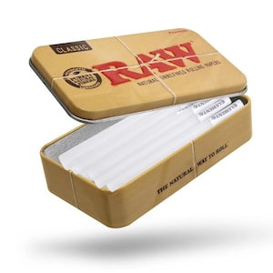 K&ouml;nnte beinhalten: Eine beige Metallbox mit dem Wort "RAW" in Rot, die wei&szlig;e Zigarettenpapier enth&auml;lt. Der Deckel ist leicht ge&ouml;ffnet und gibt den Inhalt frei. Der Text "NATURAL UNREFINED ROLLING PAPERS" ist sichtbar.