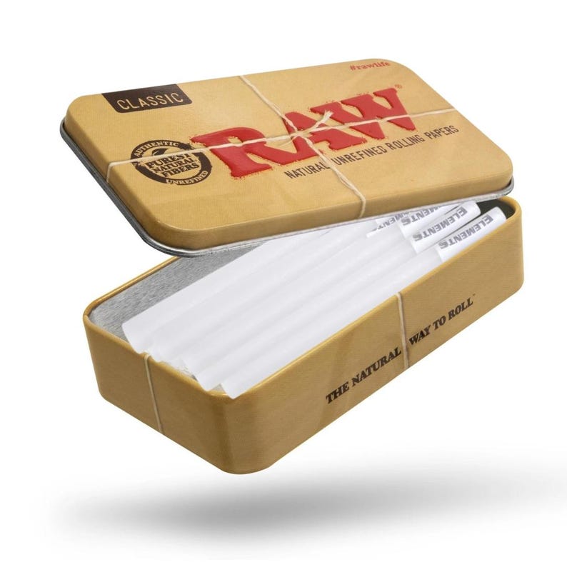 K&ouml;nnte beinhalten: Eine beige Metallbox mit dem Wort "RAW" in Rot, die wei&szlig;e Zigarettenpapier enth&auml;lt. Der Deckel ist leicht ge&ouml;ffnet und gibt den Inhalt frei. Der Text "NATURAL UNREFINED ROLLING PAPERS" ist sichtbar.
