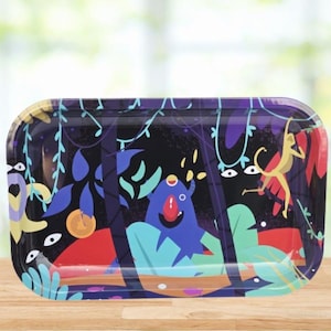 May include: A rectangular metal tray with a colorful jungle-themed design. The tray features a dark background with illustrations of cartoonish creatures, plants, and a monkey. The color palette includes blue, red, yellow, and green.