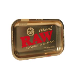 May include: A rectangular, gold-colored rolling tray with rounded corners. The tray features the red "RAW" logo and text, "PHENOMENALLY THIN ROLLING PAPER." Additional text includes "Ethereal," "CLASSIC," and "VEGAN GUM."