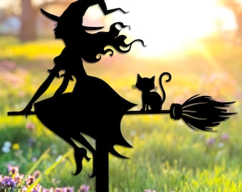 Pode incluir: Silhueta de metal preto de uma bruxa numa vassoura com um gato. A bruxa usa um chapéu pontudo e um vestido. A vassoura tem cerdas detalhadas. A estaca de jardim está num campo de flores roxas.