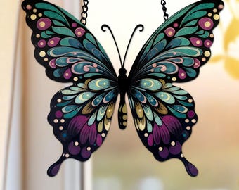 May include: A colourful butterfly decoration with detailed wing patterns in teal, purple, and pink, hanging from a black chain. The butterfly's design has a stained-glass effect, adding elegance. The background is blurred, suggesting a window setting.
