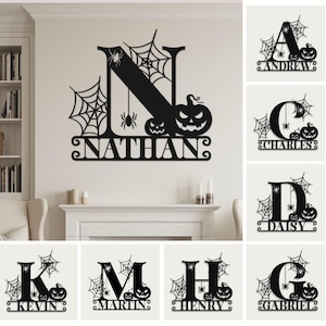 May include: Black metal Halloween-themed wall decor featuring a letter, name, spiderwebs, spiders, and jack-o'-lanterns. The name "NATHAN" is displayed below the letter "N". Additional designs include letters with names like "ANDREW", "CHARLES", and "DAISY".