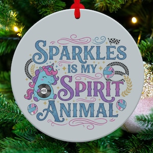 May include: A round, light gray Christmas ornament with the text "Sparkles is my Spirit Animal" in blue and purple script. A cartoon unicorn and racing-themed graphics decorate the ornament, which hangs from a red ribbon.