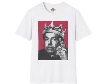 May include: White t-shirt featuring a black and white image of a person wearing a crown and rings, set against a red background. The image is centered on the shirt, showcasing a bold graphic design.