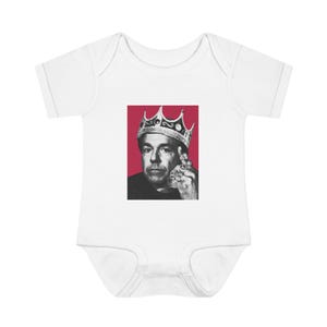 May include: White baby bodysuit featuring a black and white image of a man wearing a crown and rings, set against a red background. The bodysuit is made of soft fabric, perfect for newborns and infants.