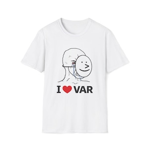 May include: White t-shirt featuring a graphic of a crying face wearing a smiling mask. The text "I ❤️ VAR" is printed below the graphic in black and red. The shirt has short sleeves and a crew neck.