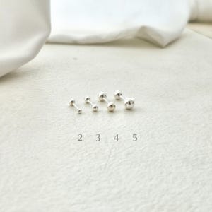 May include: A collection of five silver-colored barbell stud earrings, each with a small, round ball on either end. The earrings are arranged in a row, with the numbers 2, 3, 4, and 5 printed below them.