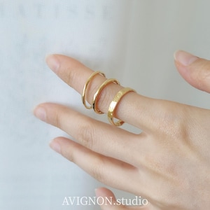 Può includere: Tre anelli color oro con una finitura liscia e lucida indossati su un dito. Gli anelli presentano un design semplice a fascia arrotondata. Il testo AVIGNON.studio è visibile nella parte inferiore dell'immagine, centrato sotto il dito.
