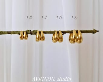 May include: Four pairs of gold hoop earrings in graduated sizes, labelled 12, 14, 16, and 18, are displayed hanging from a thin, textured branch. The earrings have a smooth, polished finish and a thick, rounded profile.
