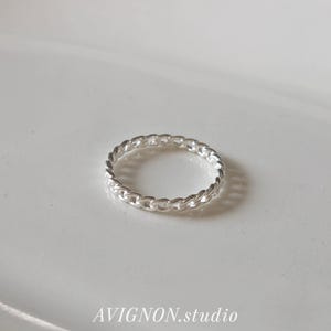 May include: A silver chain link ring. The ring is circular and features a continuous chain design. The text "AVIGNON.studio" is printed in a cursive font below the ring.