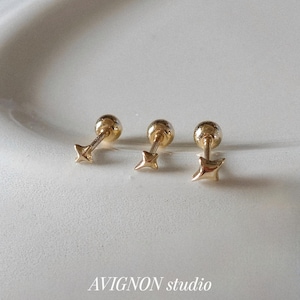 Puede incluir: Tres pendientes de oro con forma de estrella. Cada pendiente presenta una pequeña bola redonda y un diseño en forma de estrella. Los pendientes se muestran sobre una superficie blanca. El texto "AVIGNON studio" es visible.