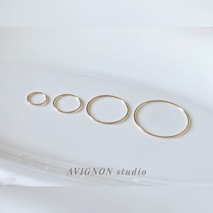 May include: Four gold-colored hoop earrings of varying sizes arranged on a white surface. The earrings are thin and circular, with a polished finish. The smallest hoop is a delicate ring, while the largest is a bold statement piece. The text "AVIGNON studio" is at the bottom.
