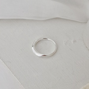 May include: A silver ring with a smooth, organic form. The ring has a slightly uneven surface, reflecting light. The design is minimalist and modern, suitable for everyday wear. The ring is shown on a white surface.