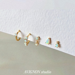 May include: A selection of gold earrings with opal gemstones. The earrings include small studs, teardrop-shaped dangles, and hoop styles. The image has the text "AVIGNON studio" in the bottom centre.
