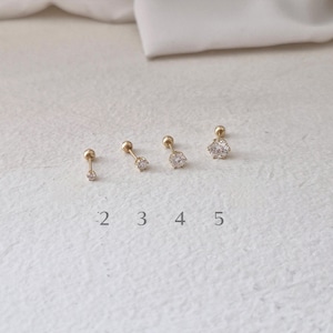 May include: Four gold stud earrings with clear cubic zirconia stones in round and flower shapes. The earrings are arranged in a row, with numbers 2, 3, 4, and 5 below them. The earrings are on a white surface.