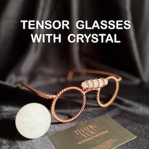 Pode incluir: Óculos com armação de arame cor de cobre com um detalhe de cristal transparente. Os óculos têm lentes redondas e são exibidos com uma esfera branca e um cartão de agradecimento. O texto "TENSOR GLASSES WITH CRYSTAL" está no topo da imagem.