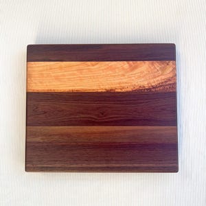 Op de afbeelding: Een rechthoekige houten snijplank met een donkerbruine walnotenbasis, een lichtbruine kersenhouten streep en een donkerbruine walnoten bovenkant. De houtnerf is zichtbaar en toont de natuurlijke patronen en texturen van het hout.