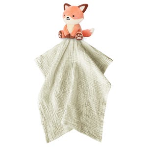 May include: A plush fox toy in shades of orange, brown, and cream sits atop a soft, light green muslin security blanket. The fox has a friendly expression and is designed for babies and young children.