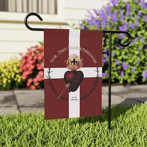 May include: A burgundy garden flag with a white cross and text. The flag features a heart with flames, a crown of thorns, and the words "Cor Jesu Sacratissimum" and "In Te Confido". The flag is displayed on a black metal stand.