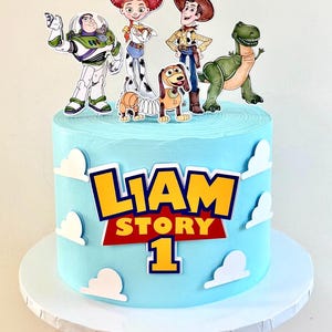 Könnte beinhalten: Eine hellblau glasierte Torte mit weißen Wolken-Ausschnitten und einem zentralen Schild mit der Aufschrift LIAM STORY 1. Obenauf befinden sich Figuren eines Weltraum-Rangers, einer Cowgirl, eines Cowboys, eines Federhundes und eines Dinosauriers.